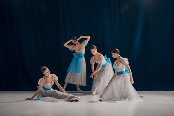 Group portrait of four ballerinas in classic white tutus and blue ribbons performing graceful...