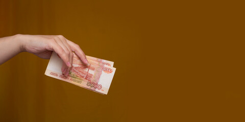 Horizontal banner. Copyspace. Female hand holds stack of red paper Russian banknotes on yellow...
