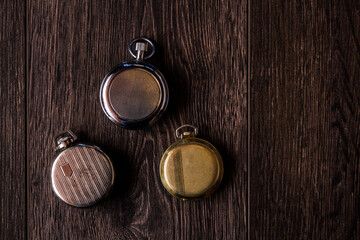 Three antique pocket watches with various designs on wooden background.