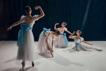 Four ballet dancers in flowing white costumes with blue ribbons, gracefully poised in different ballet positions. Concept of beauty, classic and modernity, contemporary art. Ad