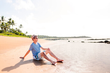 Fototapeta na wymiar A man sitting on the sandy beach, relaxing. enjoying summer vacation on a paradise beach