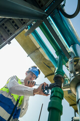 Industrial engineer adjusting pipeline valve with radio communication on construction site....