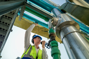 Male engineer monitoring machinery on a rooftop with city skyline in the background, wearing safety gear