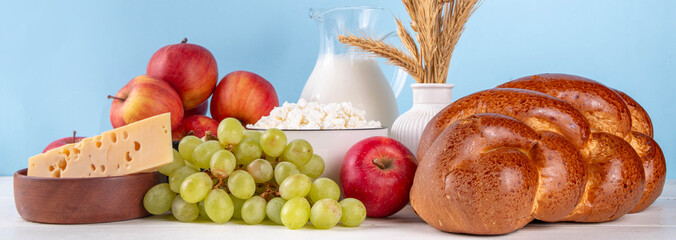 Happy Shavuot holiday background with summer red apples, wheat, grapes, dairy products - cheese,...