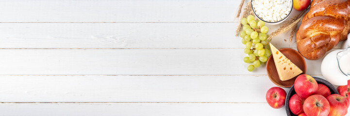 Happy Shavuot holiday background with summer red apples, wheat, grapes, dairy products - cheese, cottage cheese, milk or cream, copy space for text