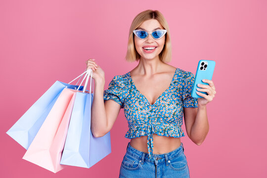 Photo of shiny attractive lady dressed blue top dark glasses chtting modern gadget holding shoppers isolated pink color background