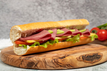 Smoked tongue sandwich on wood serving board. Sandwich made with smoked beef tongue, American salad, old cheddar cheese, tomato, cucumber and greens