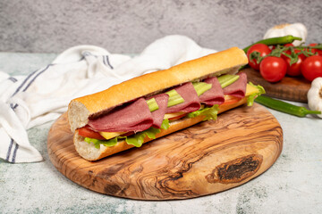 Smoked tongue sandwich on wood serving board. Sandwich made with smoked beef tongue, American salad, old cheddar cheese, tomato, cucumber and greens