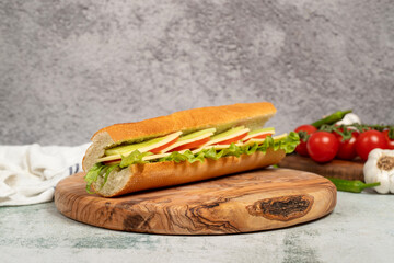 Cheddar sandwich on wood serving board. Sandwich made with tomatoes, cucumber, greens, cheddar cheese and special sauce