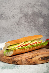Cheddar sandwich on wood serving board. Sandwich made with tomatoes, cucumber, greens, cheddar cheese and special sauce