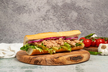 Tuna sandwich on wood serving board. Sandwich made with tuna meat, special sauce, purple onion, pickles and greens