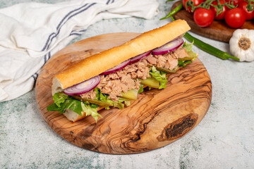 Tuna sandwich on wood serving board. Sandwich made with tuna meat, special sauce, purple onion, pickles and greens