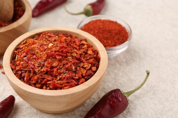 Chili pepper flakes and pods on light textured table, closeup. Space for text