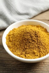 Dry curry powder in bowl on wooden table, closeup