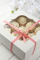 Tasty cupcakes with vanilla cream in box and orchid flowers on white wooden table, closeup