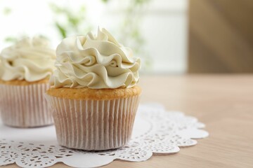 Tasty cupcakes with vanilla cream on light wooden table, closeup