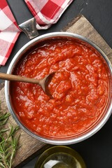 Homemade tomato sauce in pot, spoon and fresh ingredients on dark table, flat lay