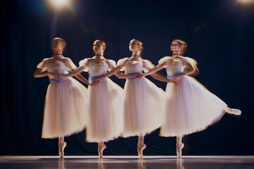 Charming young girls, ballet dancers in white tutus with blue bows on pointe dancing in motion on...