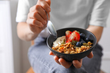 Woman eating tasty granola with berries, yogurt and seeds indoors, closeup