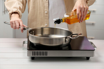 Vegetable fats. Woman pouring cooking oil into frying pan on stove in kitchen, closeup
