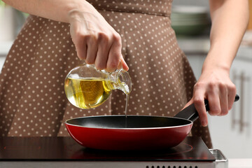 Vegetable fats. Woman pouring cooking oil into frying pan on stove in kitchen, closeup