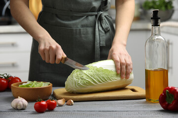 Woman cutting fresh chinese cabbage at grey wooden table in kitchen, closeup