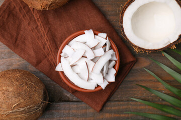 Coconut pieces in bowl, nuts and palm leaf on wooden table, flat lay