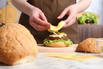 Woman making delicious vegetarian burger at white marble table, closeup