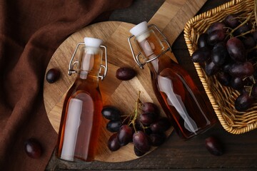 Bottles with wine vinegar and grapes on wooden table, flat lay