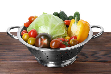 Metal colander with different vegetables on wooden table against white background