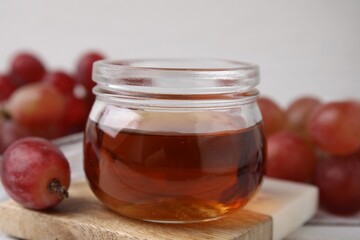 Wine vinegar in glass jar and grapes on table, closeup