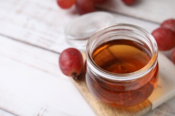 Wine vinegar in glass jar and grapes on light wooden table, closeup. Space for text