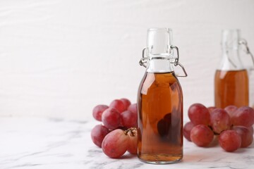 Wine vinegar in glass bottles and grapes on white marble table, space for text