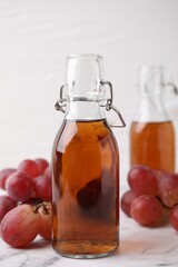 Wine vinegar in glass bottles and grapes on white marble table