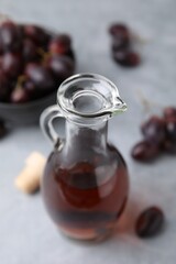 Wine vinegar in glass jug and grapes on grey table, closeup