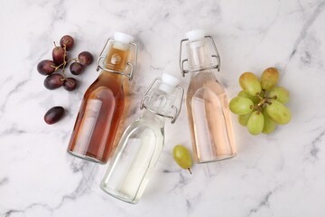 Different types of vinegar in bottles and grapes on light marble table, flat lay