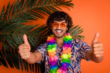 Photo of attractive young man thumb up enjoy summer palm leaves dressed stylish colorful clothes isolated on orange color background