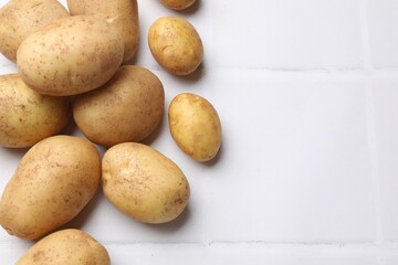 Raw fresh potatoes on white tiled table, top view. Space for text