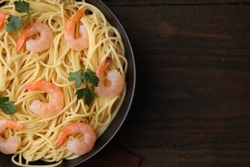 Tasty spaghetti with shrimps and parsley in bowl on wooden table, top view. Space for text