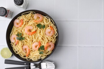 Tasty spaghetti with shrimps and parsley in bowl served on light tiled table, flat lay. Space for...