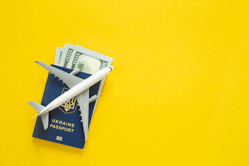 Ukrainian biometric passport, money and airplane on a yellow background.