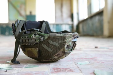 Military mission. Camouflage helmet on floor inside abandoned building, closeup