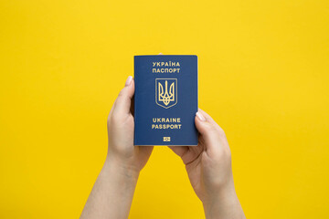 Passport of a citizen of Ukraine in a female hand on a yellow background.