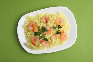 Delicious risotto with shrimps, lime and parsley on light green background, top view