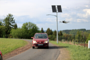 Dron w locie, w powietrzu, w tle panele słoneczne z latarnią uliczną, samochody osobowe na drodze. © Stanisław Błachowicz