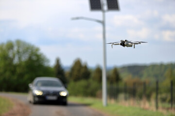 Dron w locie, w powietrzu, w tle panele słoneczne z latarnią uliczną, samochody osobowe na drodze. © Stanisław Błachowicz