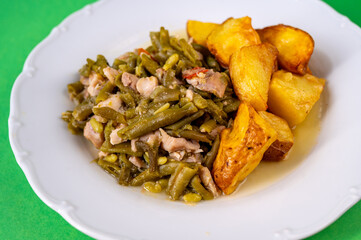 Green beans with tuna fish piece and baked potato on white plate.