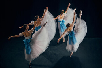 Four ballerinas in white and blue costumes performing on stage, each dancer showcasing exquisite...