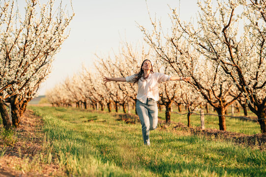 Cheerful young woman in jeans is running free through an almond orchard.
