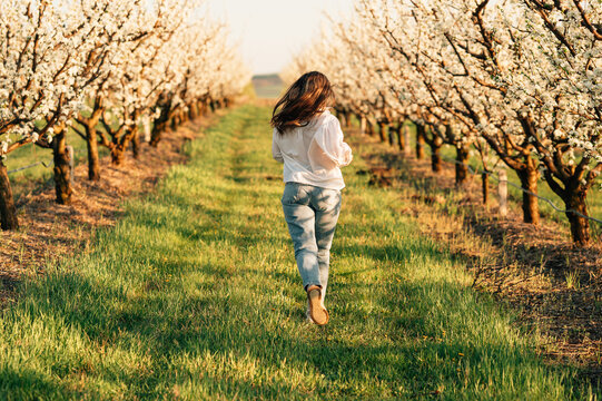 Playful cheerful young woman in jeans is running through an almond orchard.